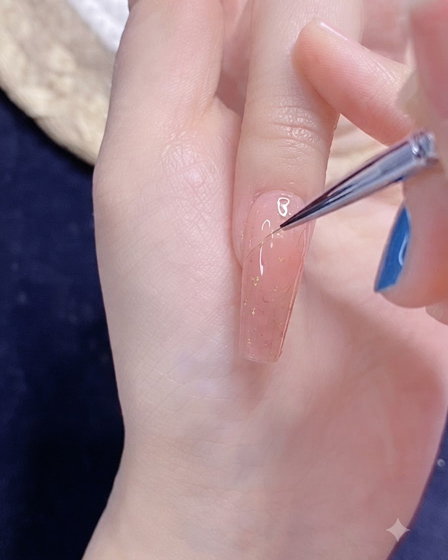 Ein feiner Nail-Art-Pinsel zeichnet eine filigrane halbe Herzumrandung mit Gel auf einen rosa lackierten Nagel.