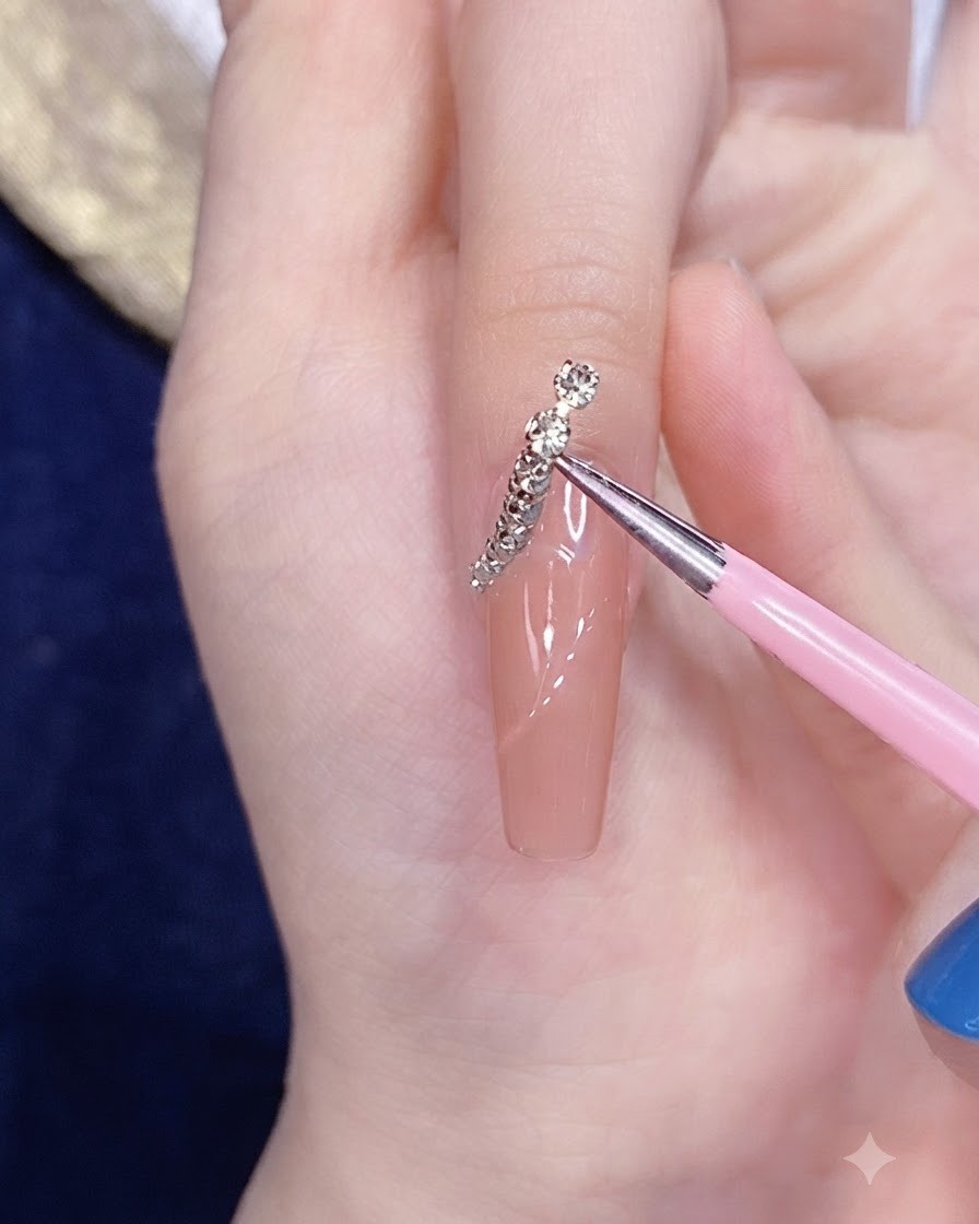 Ein feines Applikationswerkzeug platziert einen segmentierten Silber-Gold-Kettenstreifen auf die geschwungene Linie eines Nagels.