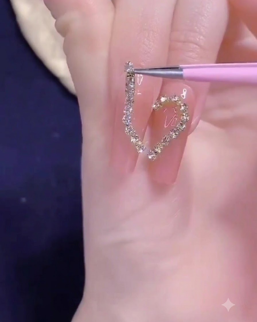 Eine Präzisionspinzette platziert einen goldenen Kettenstreifen auf das halbe Herz-Nageldesign.