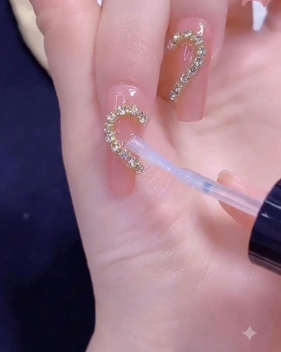 Ein Pinsel trägt Klarlack über einen goldenen Kettenstreifen auf, der in einer halben Herzform auf einem Fingernagel angeordnet ist.