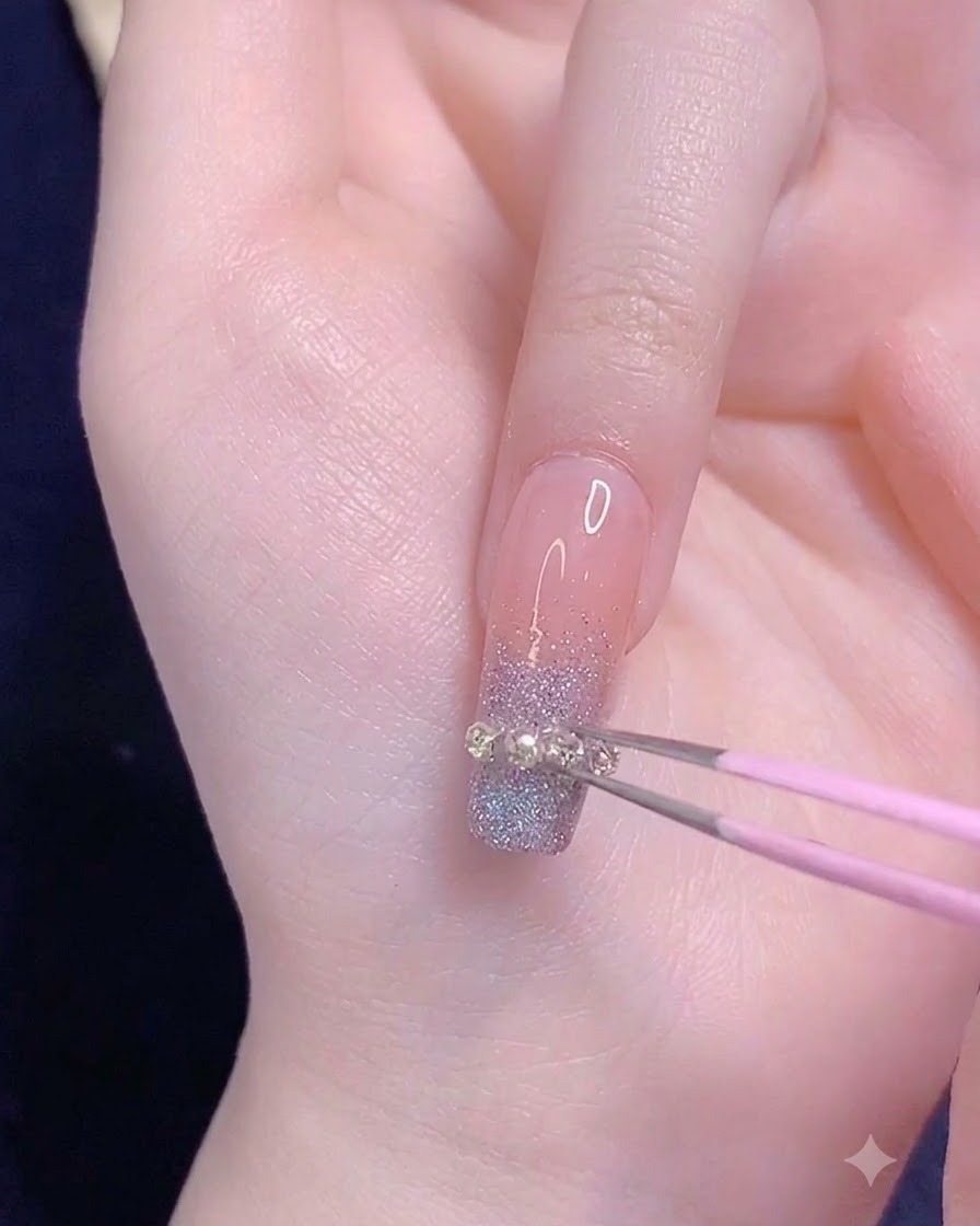 Eine rosa Pinzette platziert einen kleinen Metallkettenstreifen horizontal über der Verlaufspitze eines Ringfingernagels.