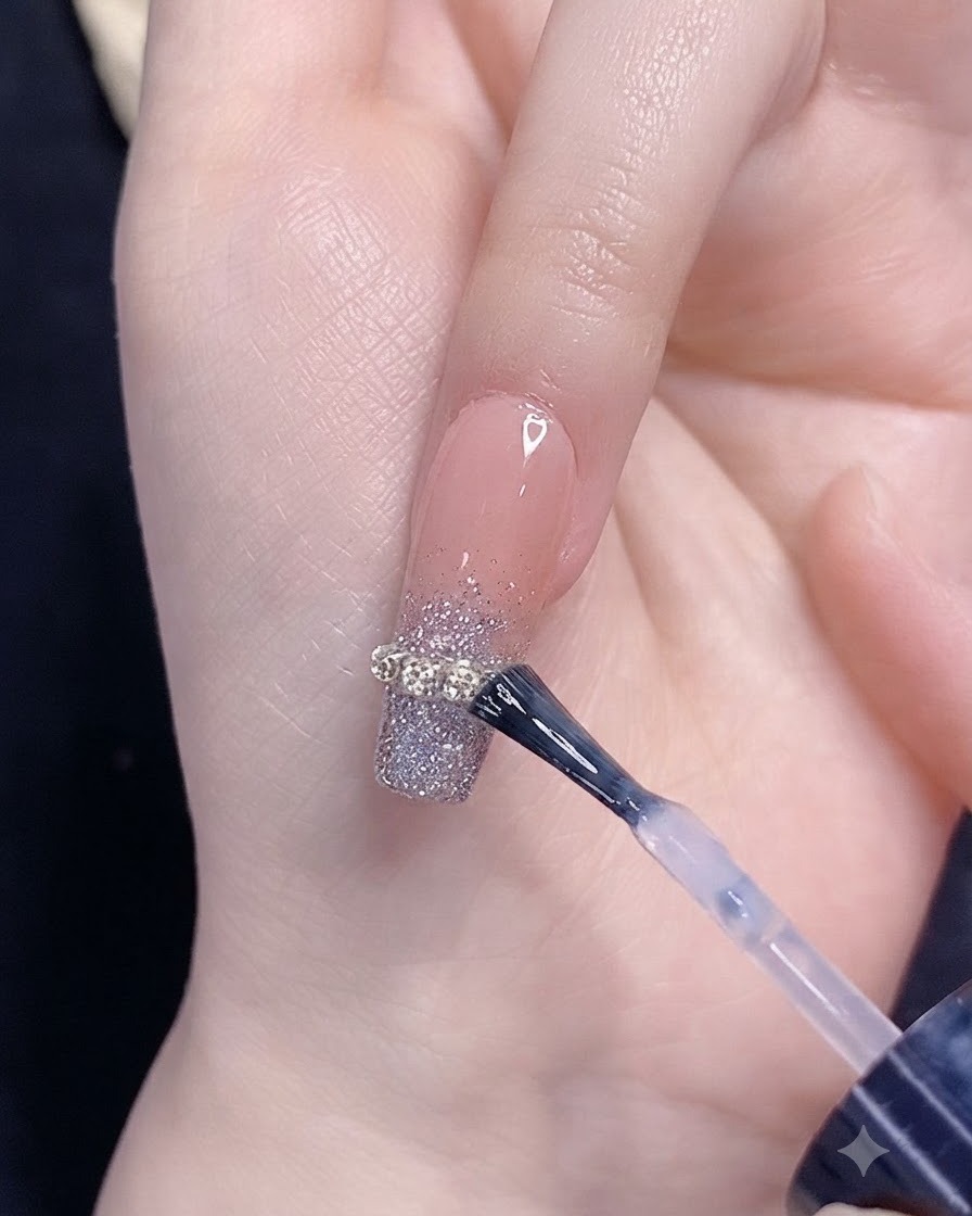 Ein Pinsel trägt Top-Coat über einen silbernen Glitzer-Verlaufsnagel mit einem Kettenstreifen-Akzent auf.