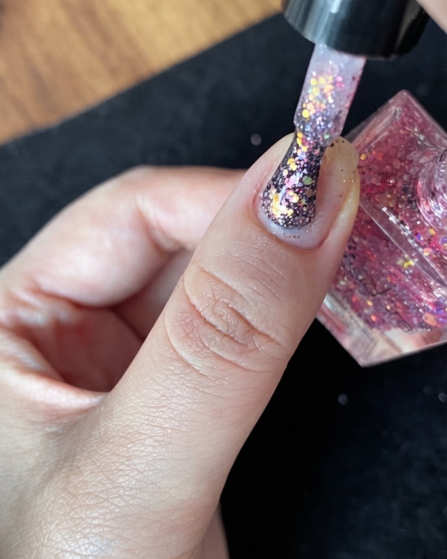 Eine Nahaufnahme eines Naturnagels mit Nude-Basisschicht und spärlich verteilten Glitzerflocken.