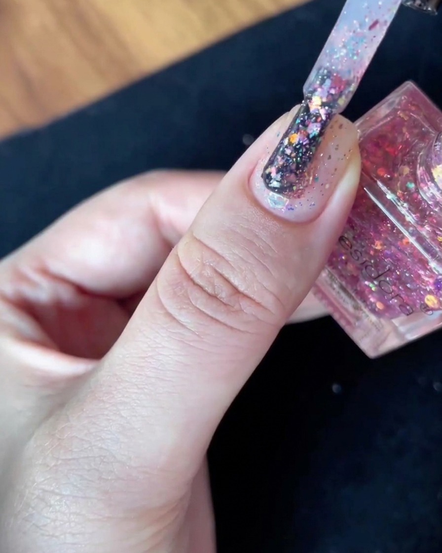 Ein mit Glitzerflocken gefüllter Lackierpinsel wird ruhig direkt über der Oberfläche eines Nude-Nafels gehalten.