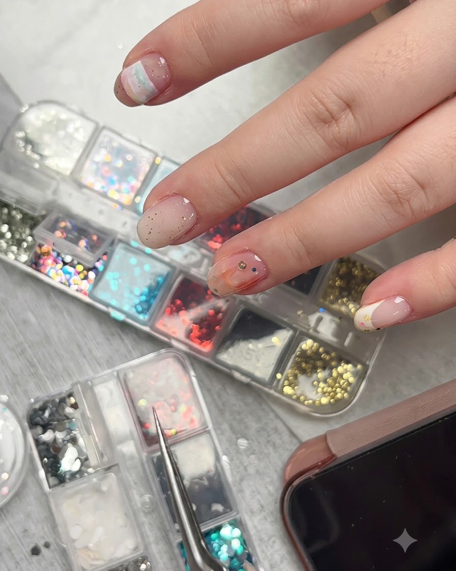 Eine Pinzette hält ein winziges Stern-Glitterstück knapp über einer dekorierten Nageloberfläche mit verschiedenen Akzenten.