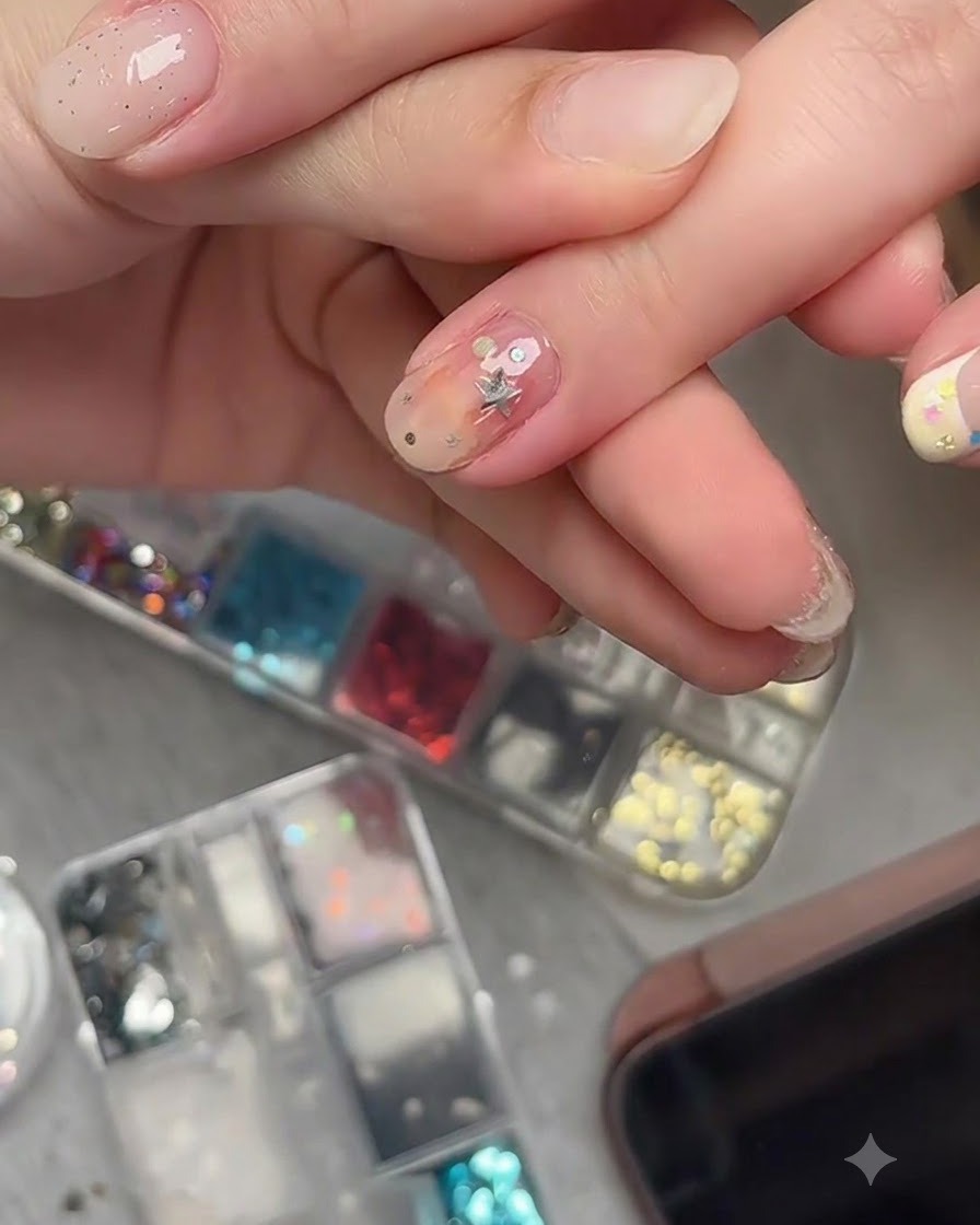 Ein Nagelkunstpinsel trägt einen klaren Überlack über eingebettete Stern-Glitterteile auf einem fertigen Nagel auf.