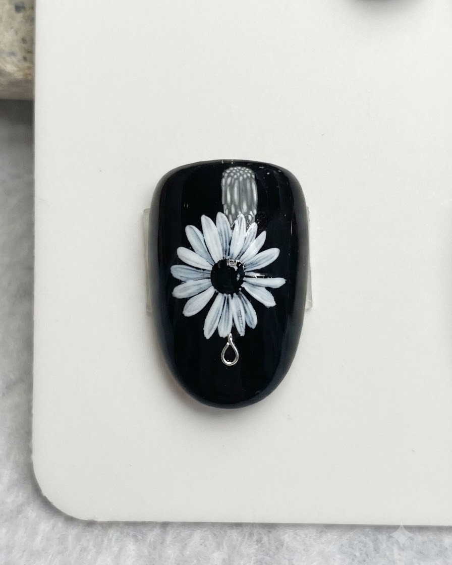 Nahaufnahme eines Nagelpinsels, der zarte weiße und gelbe Punkte auf das schwarze Zentrum eines weißen Gänseblümchen-Nagelkunstdesigns malt.