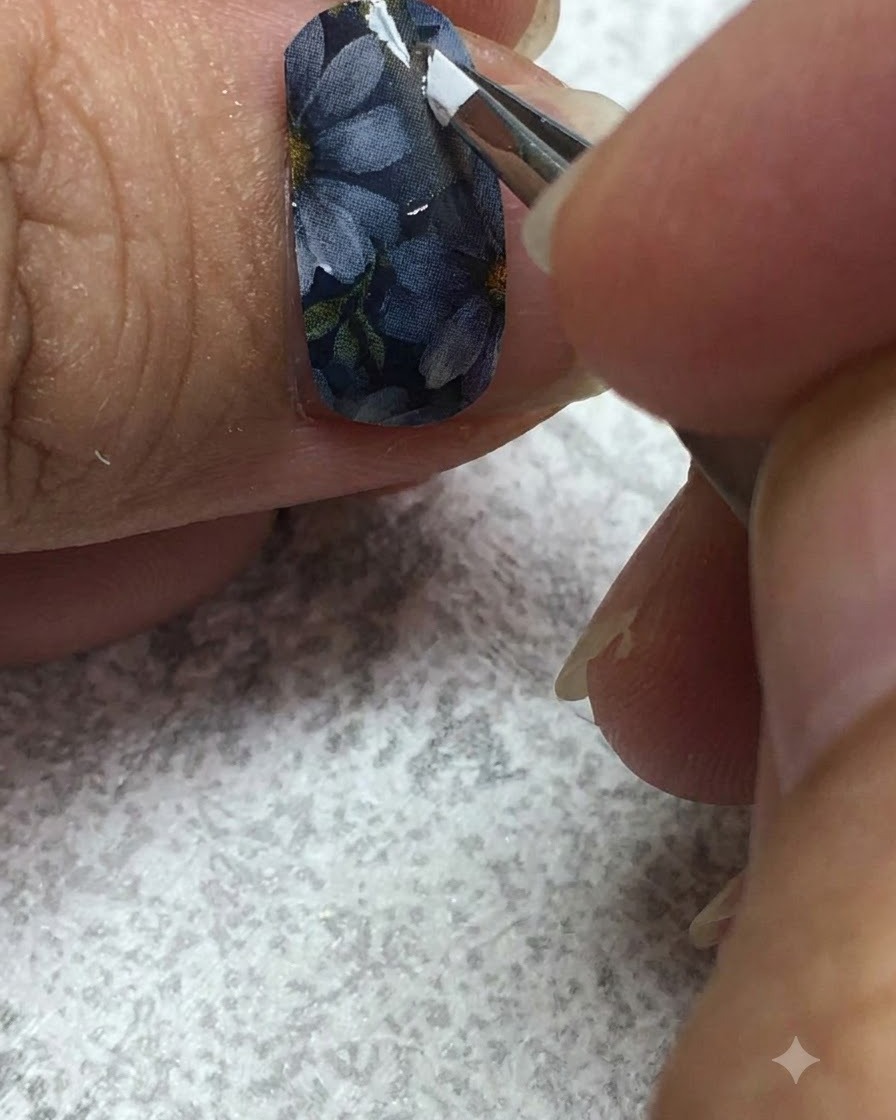 Ein feiner Liner-Pinsel, der sorgfältig weißes Gel auf die Blütenblätter eines Gänseblümchens auf einem grauen Nagel aufträgt.