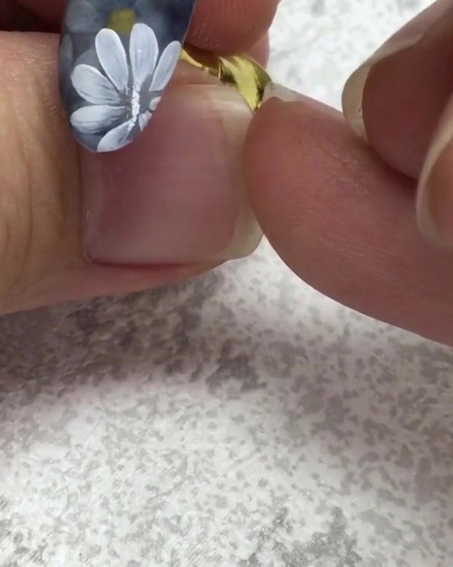 Ein flacher Nagelpinsel nimmt einen kleinen Punkt grünes Gel in der Nähe eines Nagels mit weißen Gänseblümchen auf.