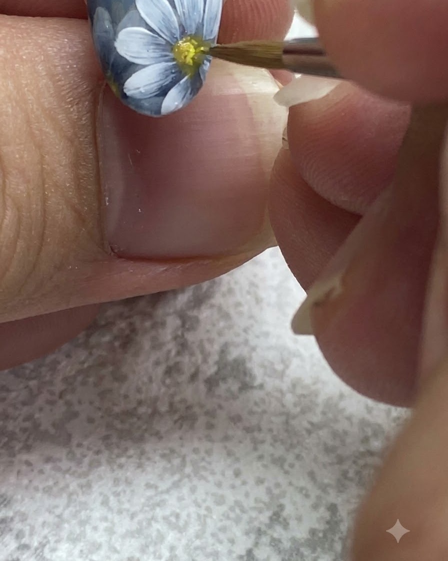 Ein feiner Pinsel tupft gelbes Gel in die Mitte eines gemalten weißen Gänseblümchens.