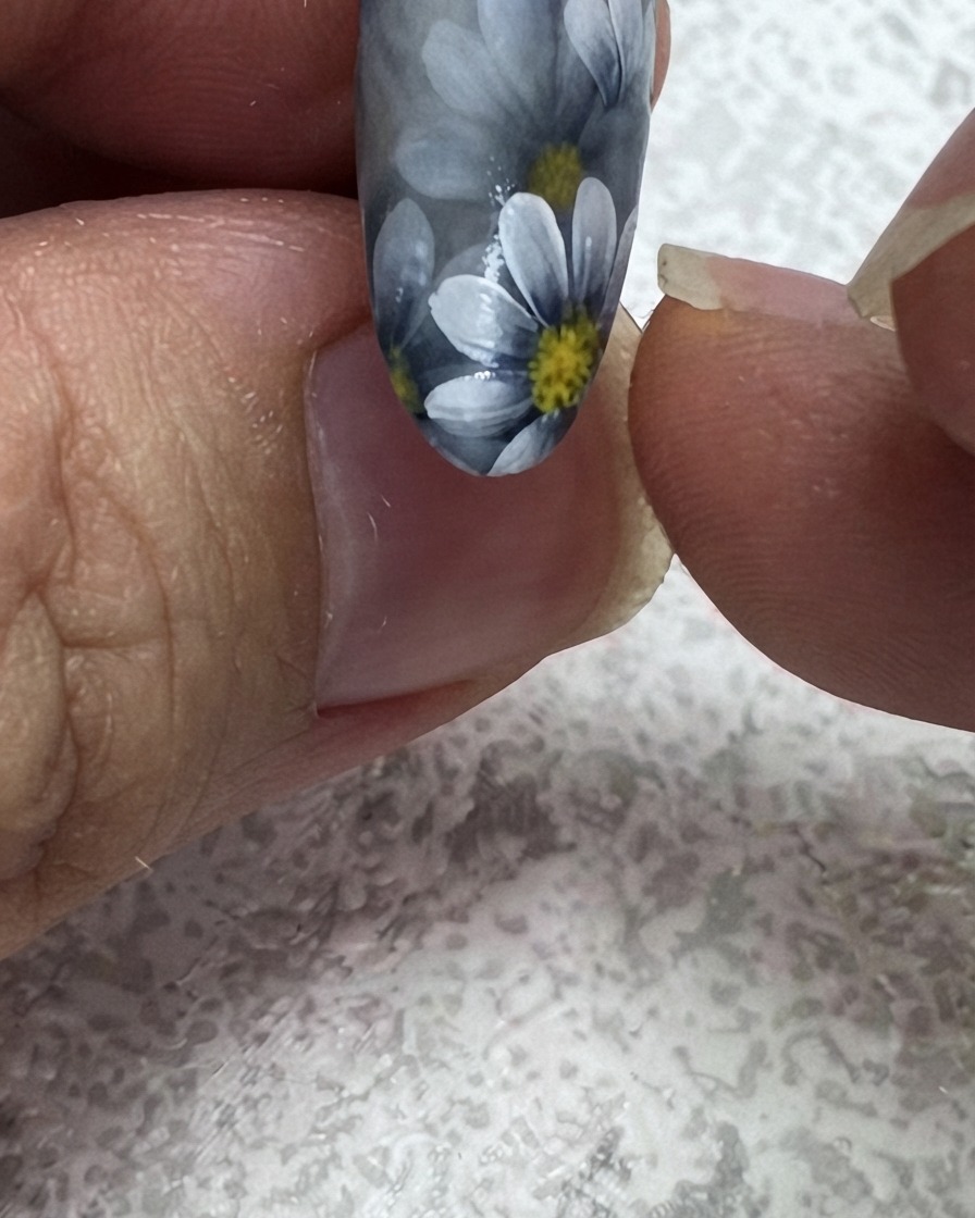 Ein feiner Liner-Pinsel fügt ein zweites grünes Blatt in der oberen Ecke eines Blumen-Nageldesigns hinzu.