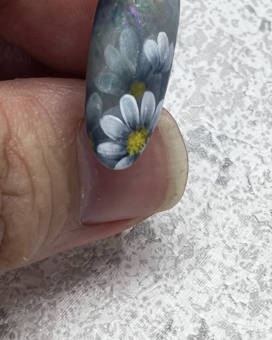 Nahaufnahme eines Nagelpinsels, der nach außen zieht, um eine scharfe Blattspitze neben gemalten Gänseblümchen im nordischen Stil zu erzeugen.