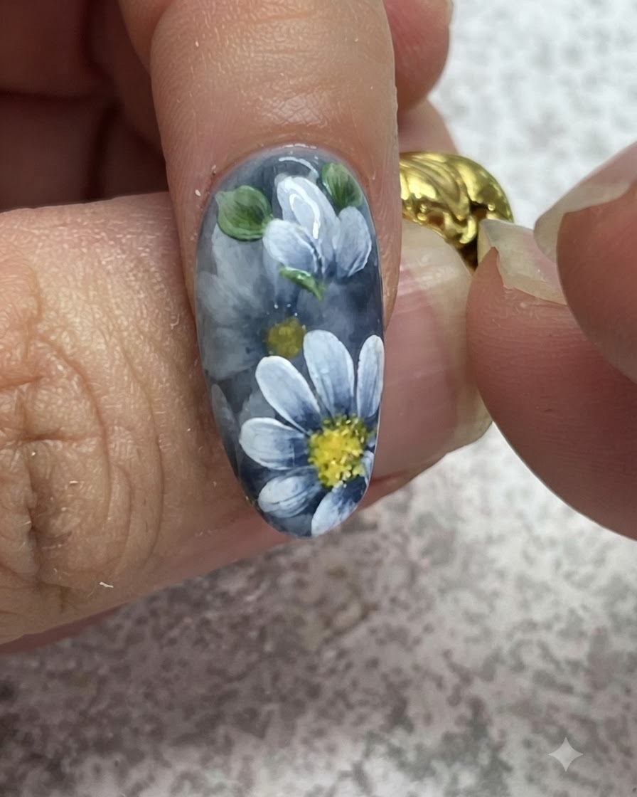 Ein feiner Pinsel setzt detailreiche Glanzlichter auf gemalte grüne Blätter bei einer grauen Gel-Maniküre.