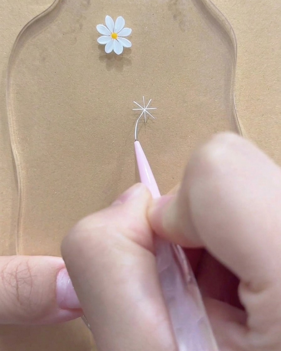 Eine Nahaufnahme eines Fine-Liner-Pinsels, der die äußeren Spitzen einer weißen Gänseblümchenblüte perfektioniert.
