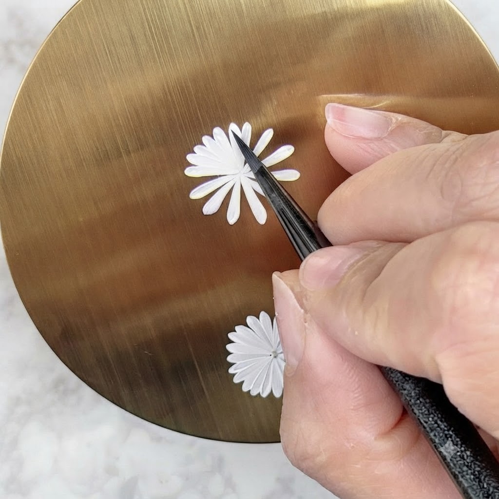 Ein Nail-Art-Pinsel bemalt sorgfältig eine zweite, kleinere innere Schicht weißer Blütenblätter auf einem Gänseblümchen-Design.
