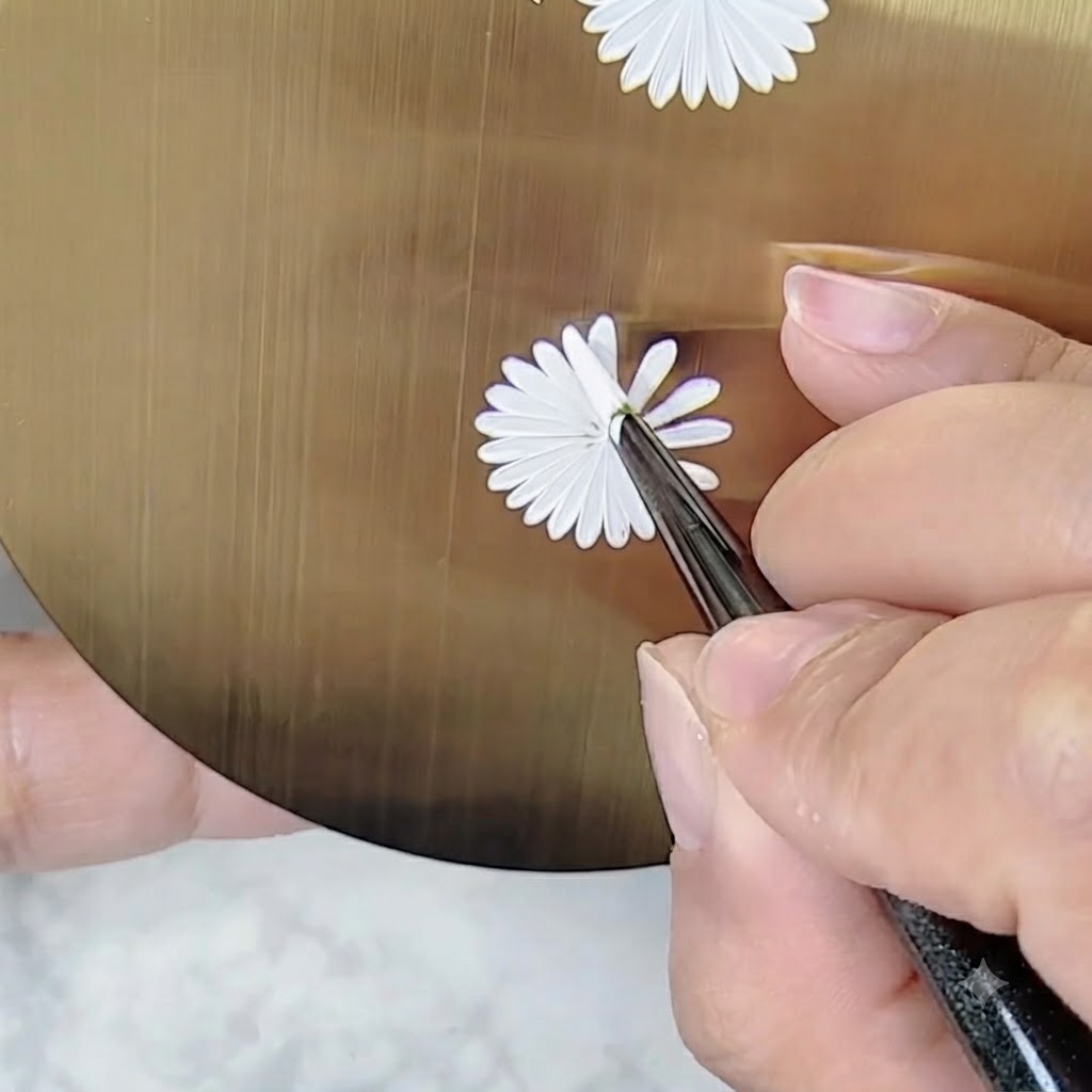 Eine Hand hält einen Nail-Art-Pinsel in einem angepassten Winkel, um Details auf einem Gänseblümchen-Design zu malen, ohne die Palette zu drehen.