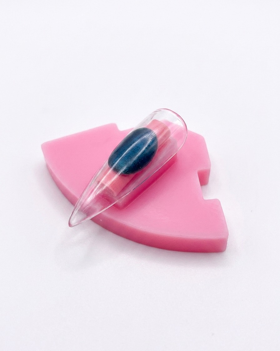 Eine einzelne Nagelspitze aus Kunststoff mit Aurora-Chrome-Finish, aufrecht auf einem rosa Halter präsentiert.