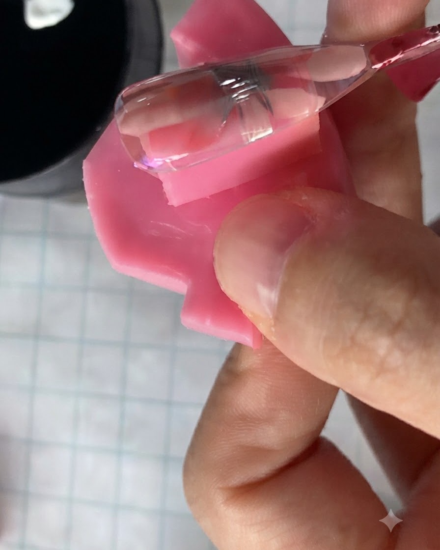 Ein kleiner Nagelpinsel trägt ein transluzentes rosa Gel über ein ausgehärtetes Gänseblümchen-Blumendesign auf einem Nagel auf.