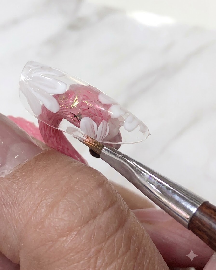 Ein Pinsel, der eine transluzente Rosagel-Polaturschicht über die gemalten weißen Blumen auf einem klaren Nagel-Tip aufträgt.