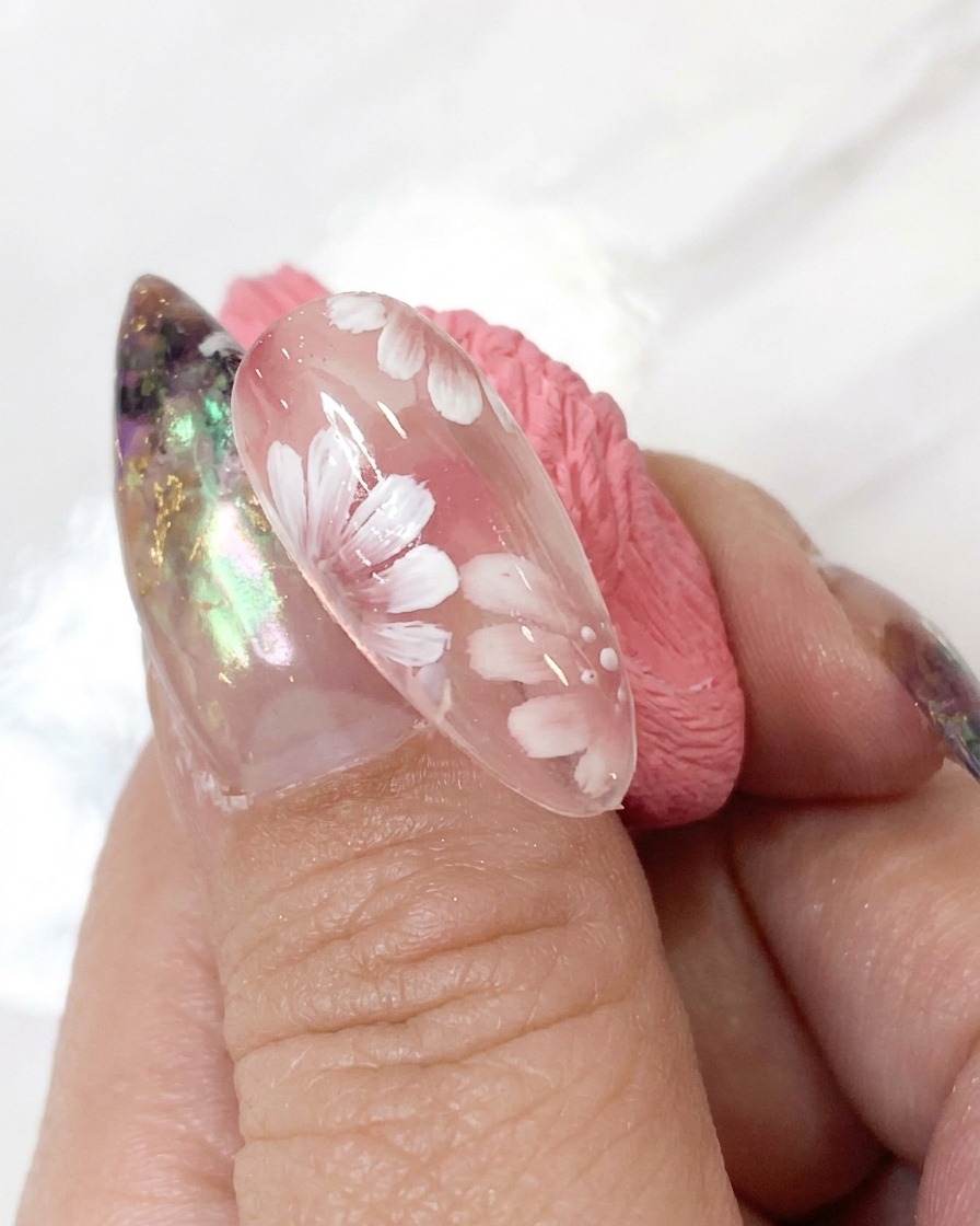 Ein Dotting-Tool, das winzige weiße Akzentpunkte um das Blumenzentrum eines detaillierten Nageldesigns aufträgt.