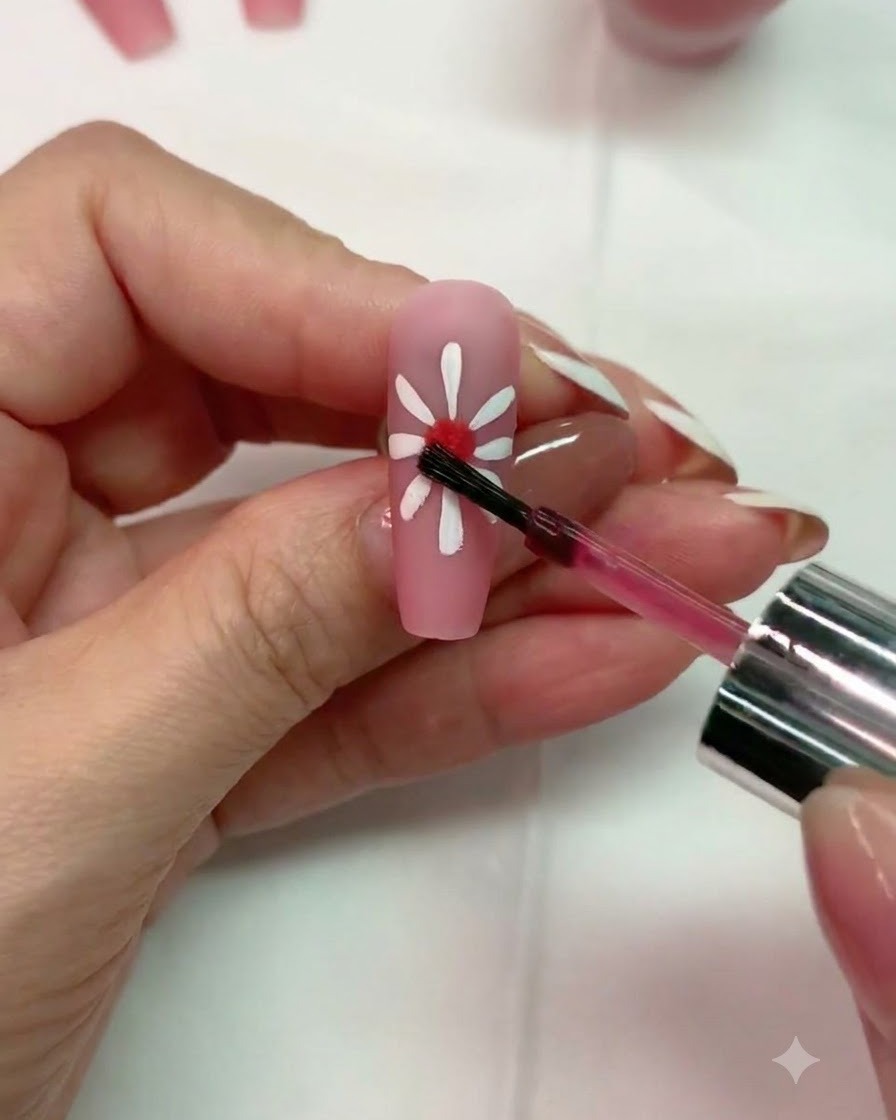 Ein Pinsel trägt einen kleinen Tropfen rotes Blooming Gel in die Mitte eines weißen Gänseblümchendesigns auf.