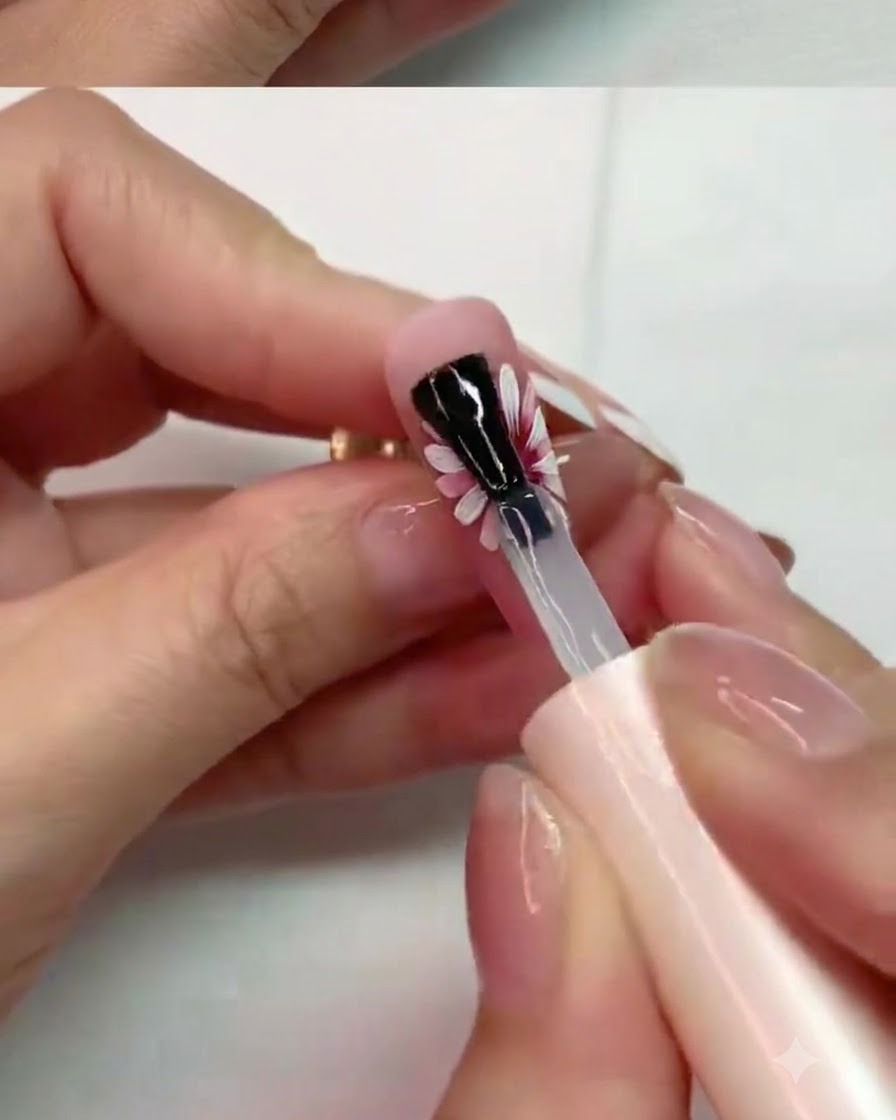 Ein Pinsel trägt vorsichtig matten Topcoat auf die mittleren Blütenblätter eines gemalten Gänseblümchendesigns auf.