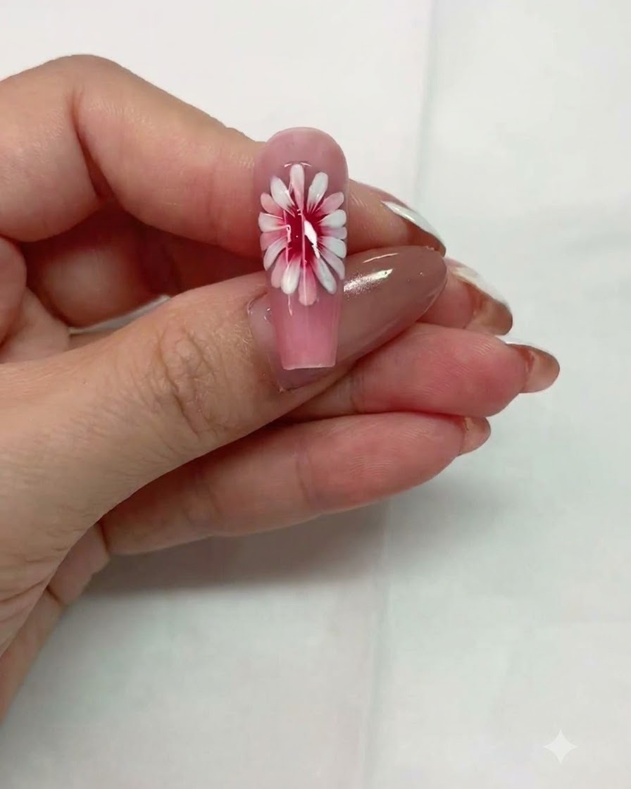 Nahaufnahme eines pinken Nagels mit mehrschichtigem Gänseblümchendesign vor dem Aushärten.