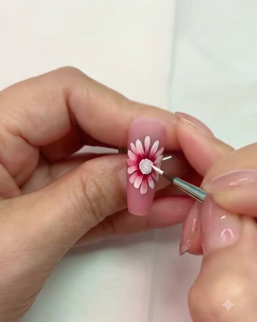 Ein feiner Pinsel arbeitet in der Nähe des ausgehärteten weißen strukturierten Zentrums der Gänseblümchen-Nagelkunst.