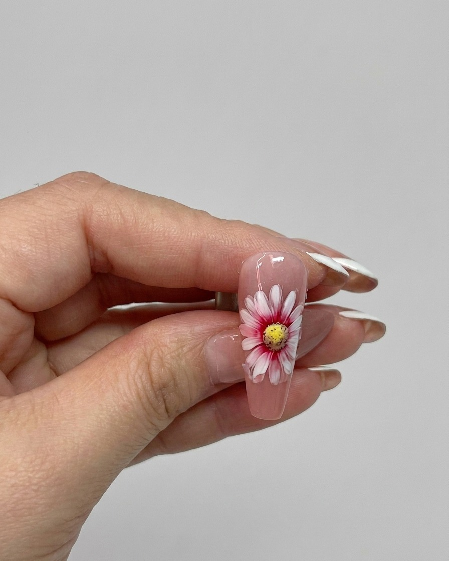 Ein Pinsel trägt einen glänzenden Topcoat über ein fertiges doppellagiges Gänseblümchen-Nageldesign auf.