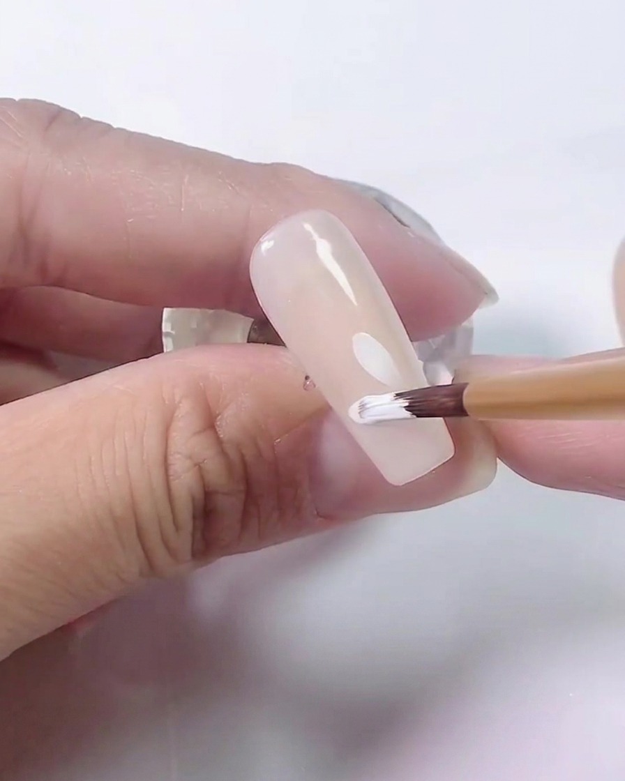Nahaufnahme eines Pinsels, der dem weißen Gänseblümchendesign auf Nude-Basis weitere Blütenblätter hinzufügt.