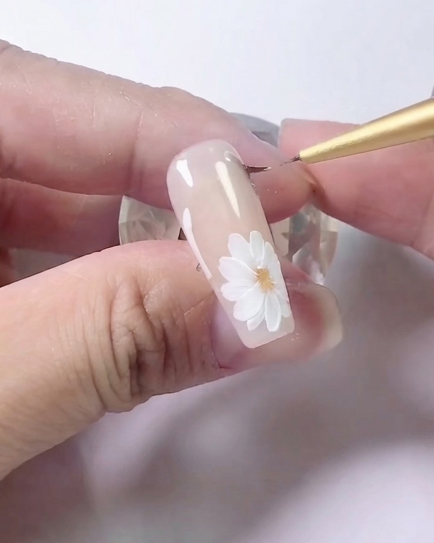 Ein Liner-Pinsel, der Grauschattierungen entlang der Seitenlinien eines floralen Nageldesigns sorgfältig verblendet.