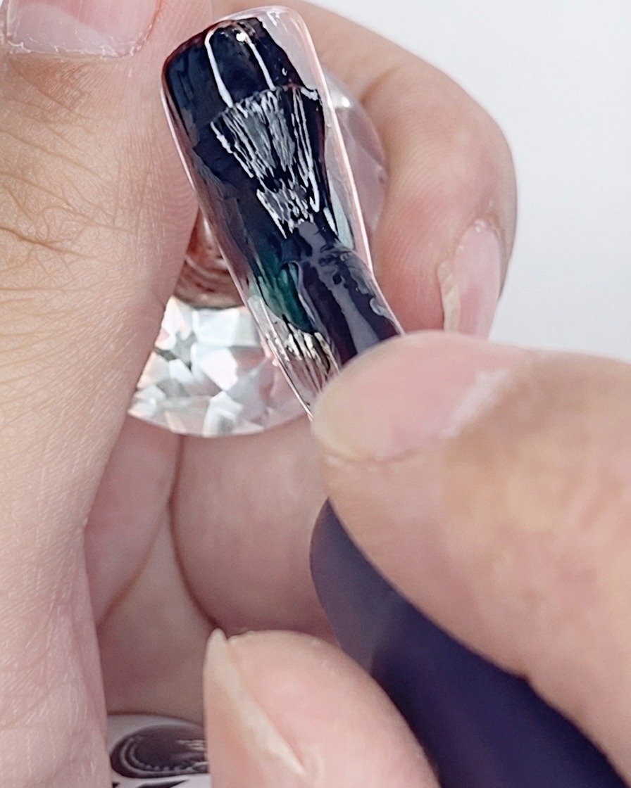 Ein Pinsel trägt die erste Schicht schwarzen Gel-Lacks auf einen künstlichen Nagel auf.