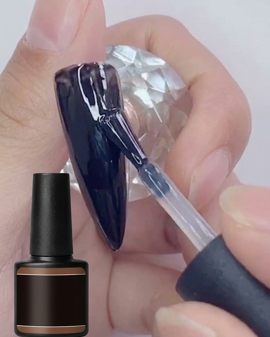Ein Pinsel trägt eine zweite Schicht glänzenden schwarzen Gel-Lacks auf einen bereits schwarz lackierten Nagel auf.