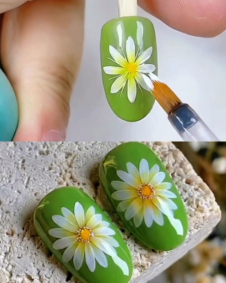 Nahaufnahme eines Pinsels, der einen glänzenden klaren Top Coat über ein weißes Gänseblümchen-Nail-Art-Design auf einem grünen Nagel aufträgt.