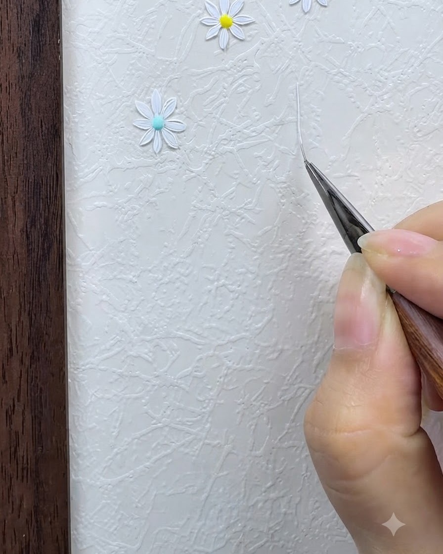 Ein Fine-Liner-Pinsel zeichnet ein dünnes, weißes, sternförmiges, sich kreuzendes Gitter auf einer strukturierten Oberfläche.