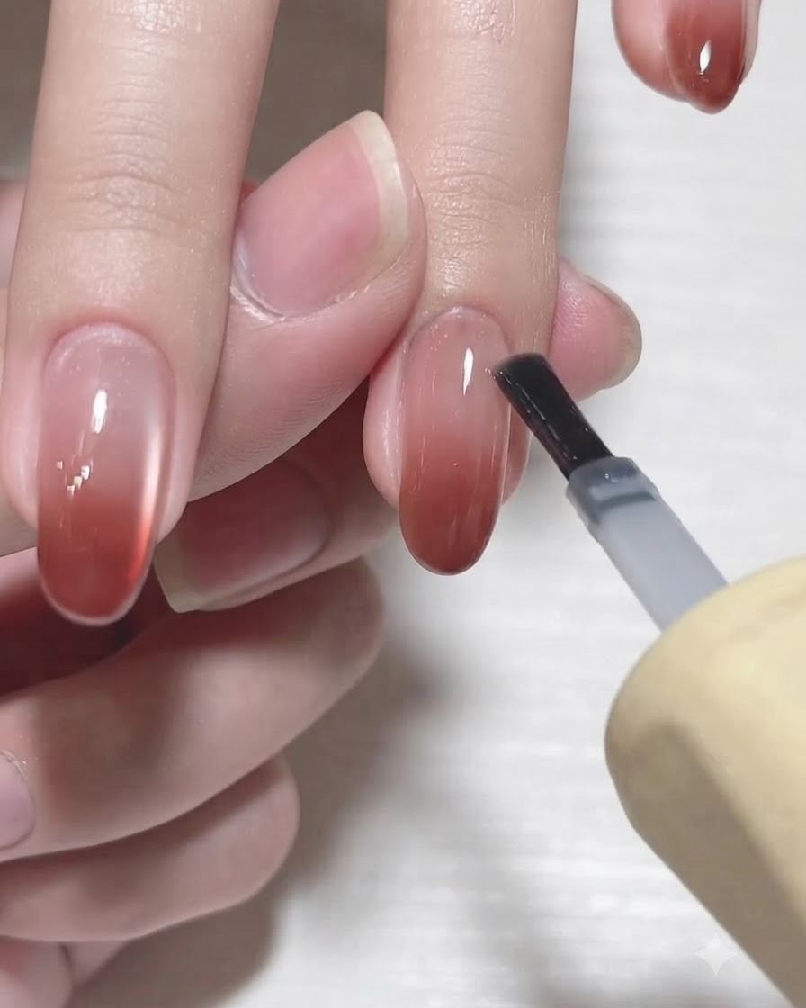 Ein Gel-Flaschenpinsel trägt einen glänzenden, klaren Überlack auf einen fertigen Farbverlaufs-Fingernagel auf.