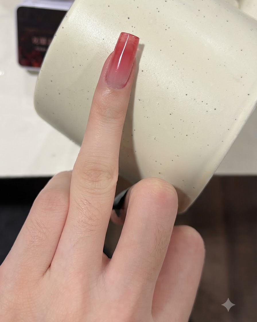 Ein Finger mit einem wachsenden weinroten Farbverlaufsnagel wird für eine zweite Schicht mit einem Schwamm getupft.