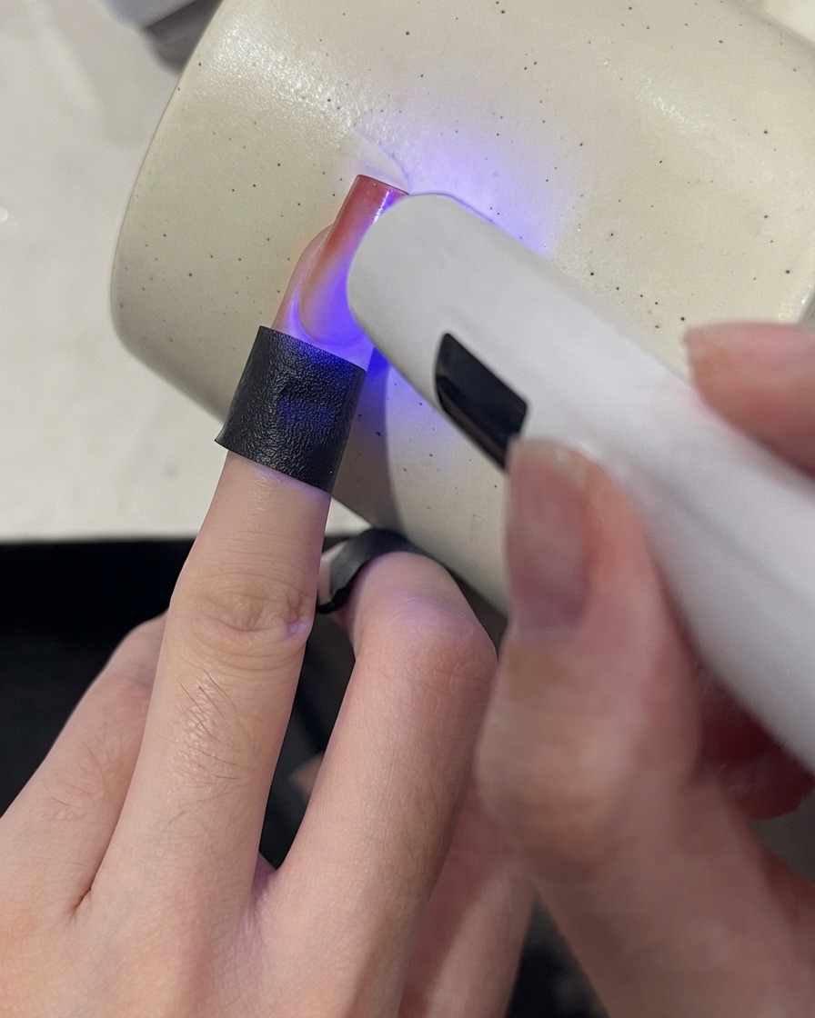 Eine Mini-UV-Lampe härtet die Spitze eines Farbverlaufsnagels mit einem weinroten Finish aus.