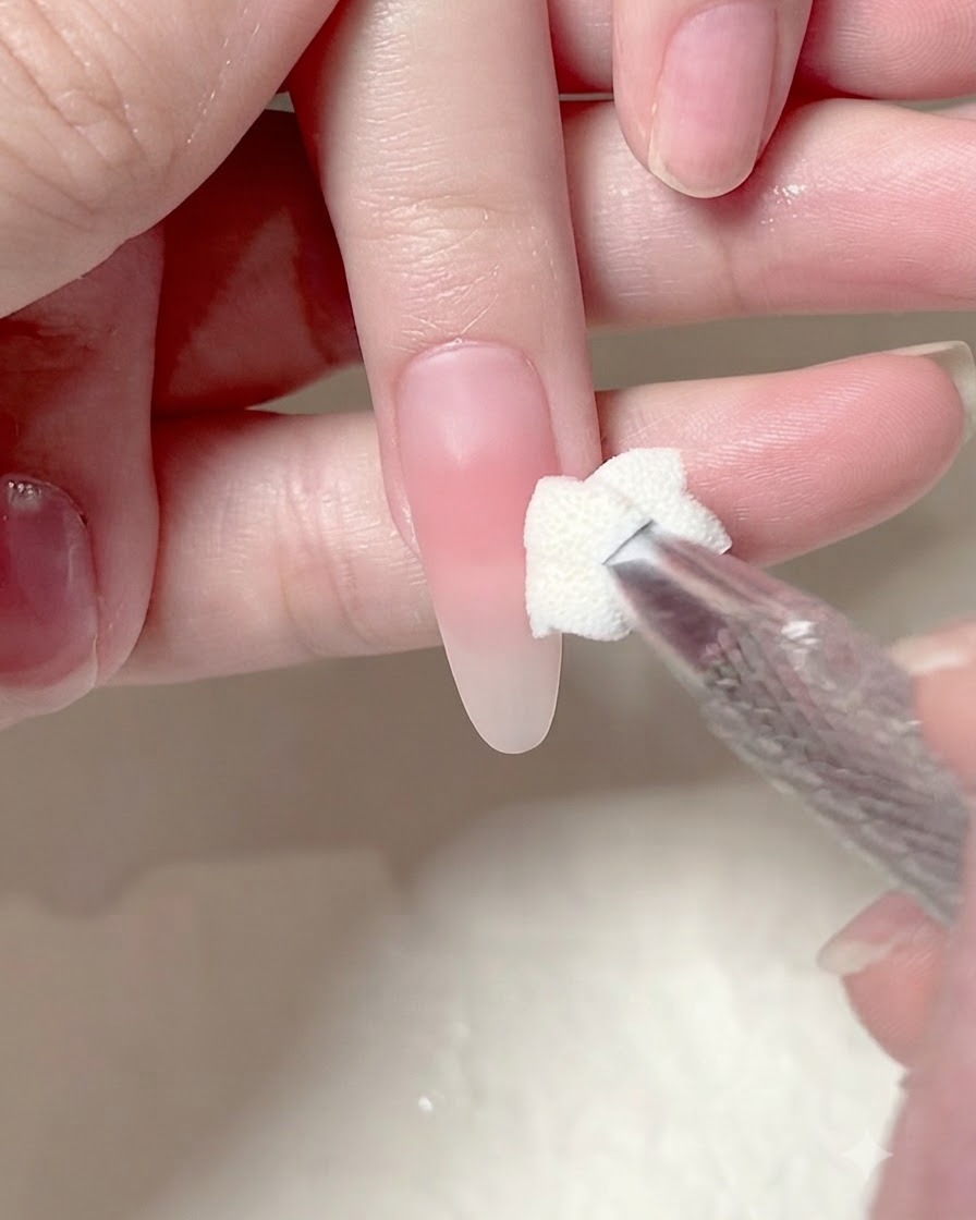 Ein Schwamm-Applikator tupft eine zweite Schicht rosa Gels auf die Mitte eines manikierten Nagels.