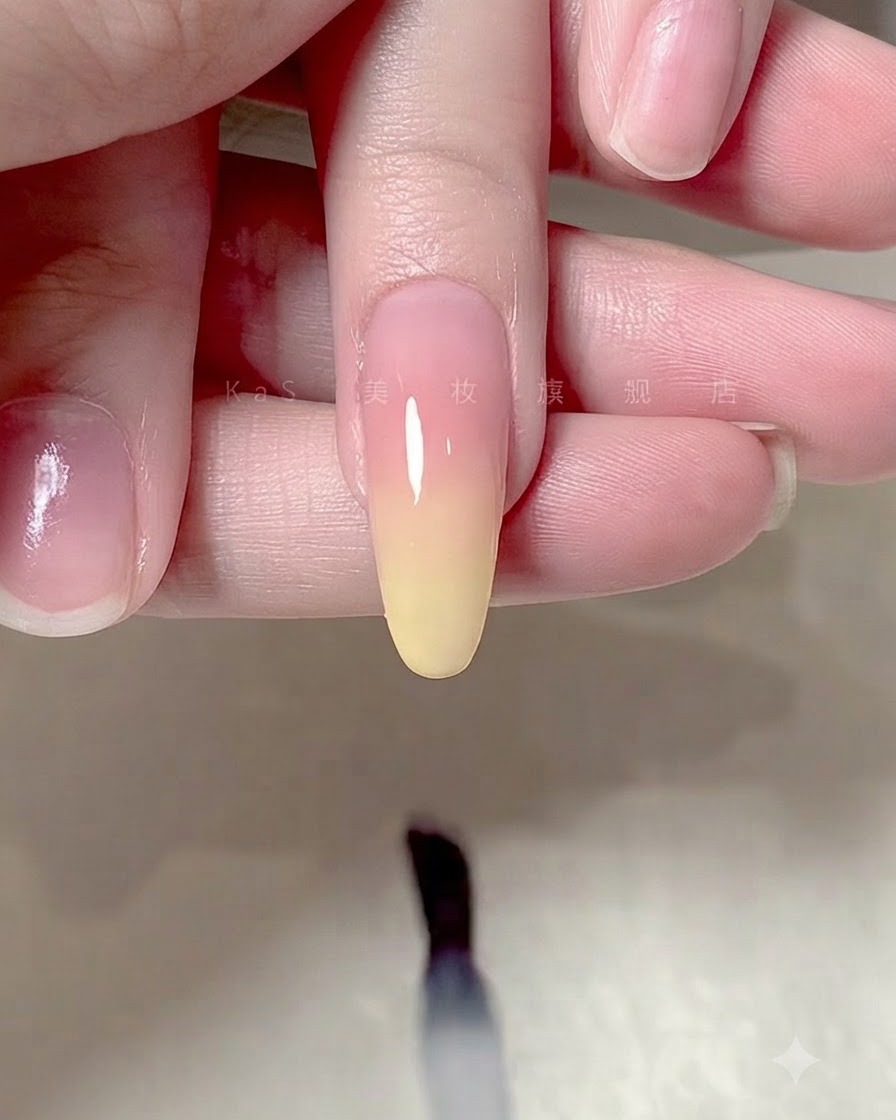Ein Pinsel trägt einen klaren, glänzenden Überzug über ein Ombre-Farbverlaufs-Nageldesign auf.