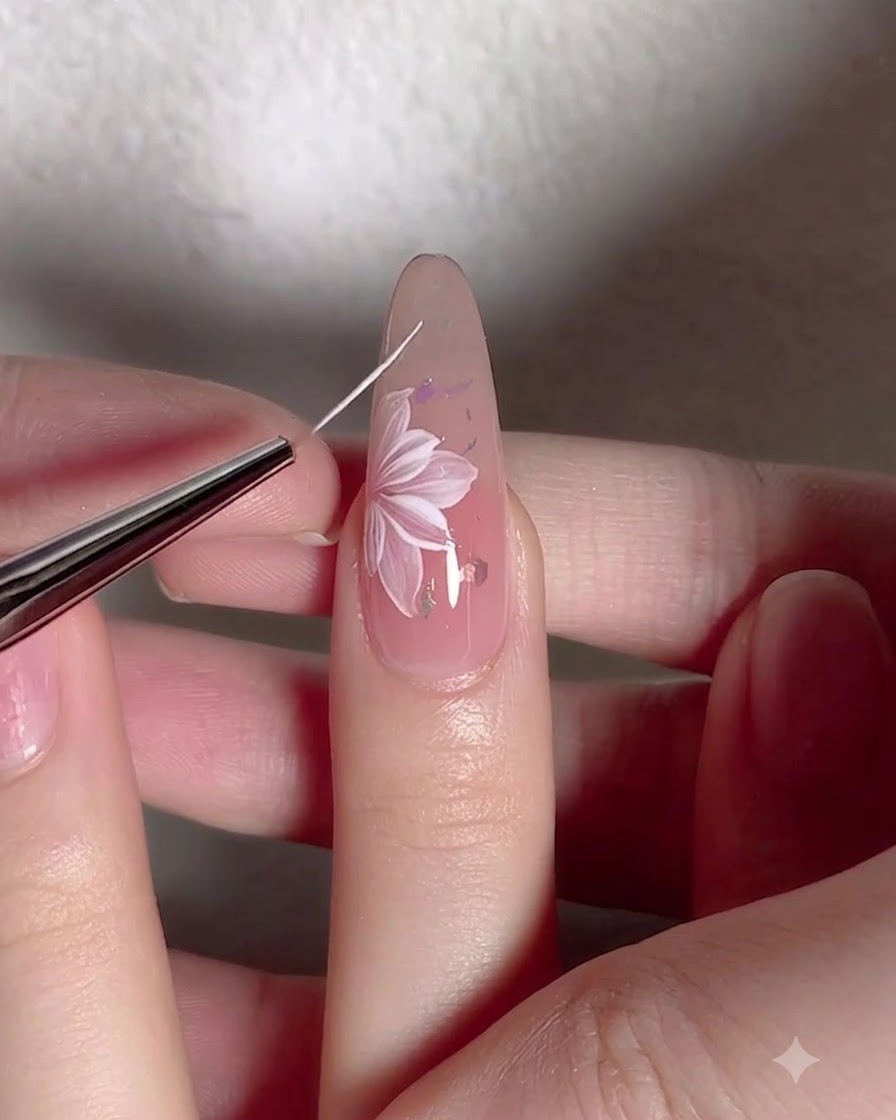 Ein feiner Liner-Pinsel zeichnet filigrane weiße Rankenlinien um eine gemalte Blume auf einem Nagel.