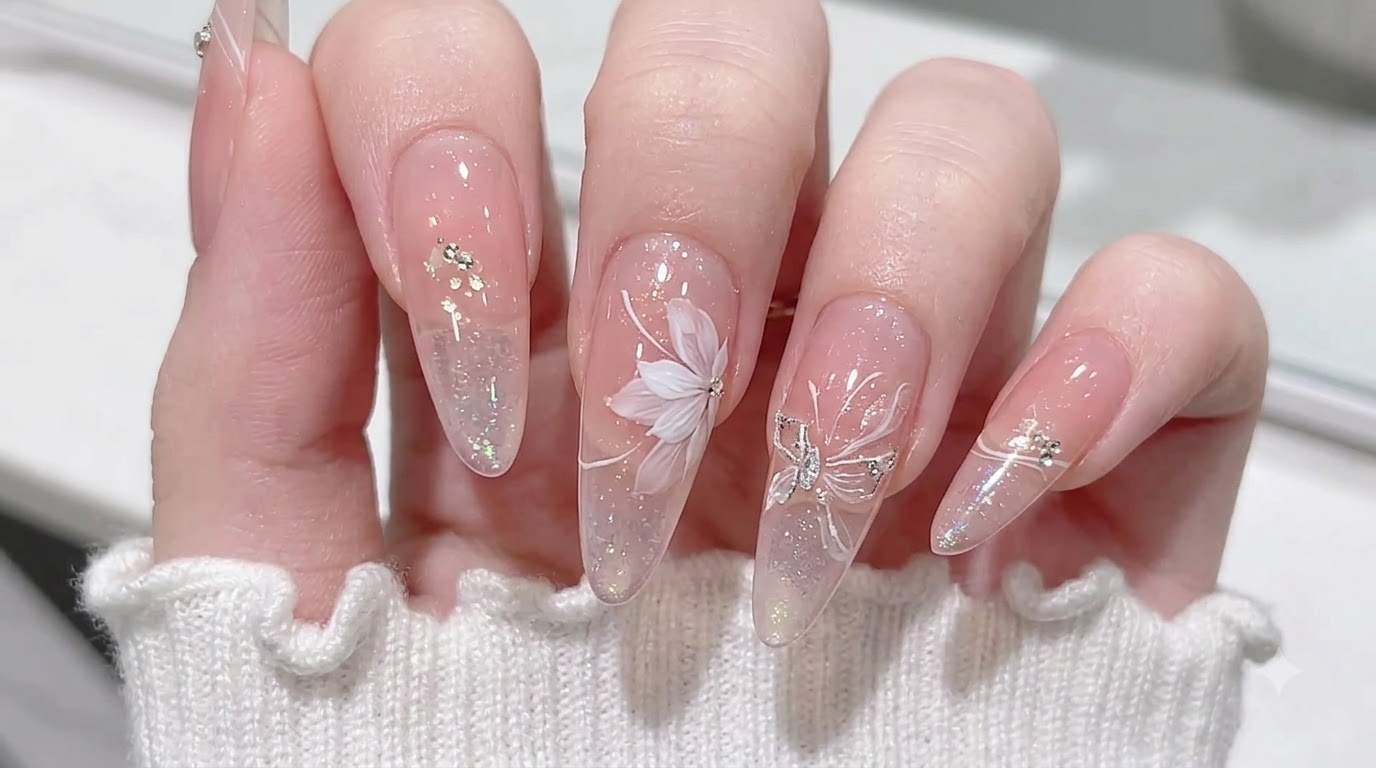 Transluzente, nude, mandelförmige Nägel mit einem rosa Blush-Verlauf, Aurora-Flocken und filigraner weißer Blumenkunst.