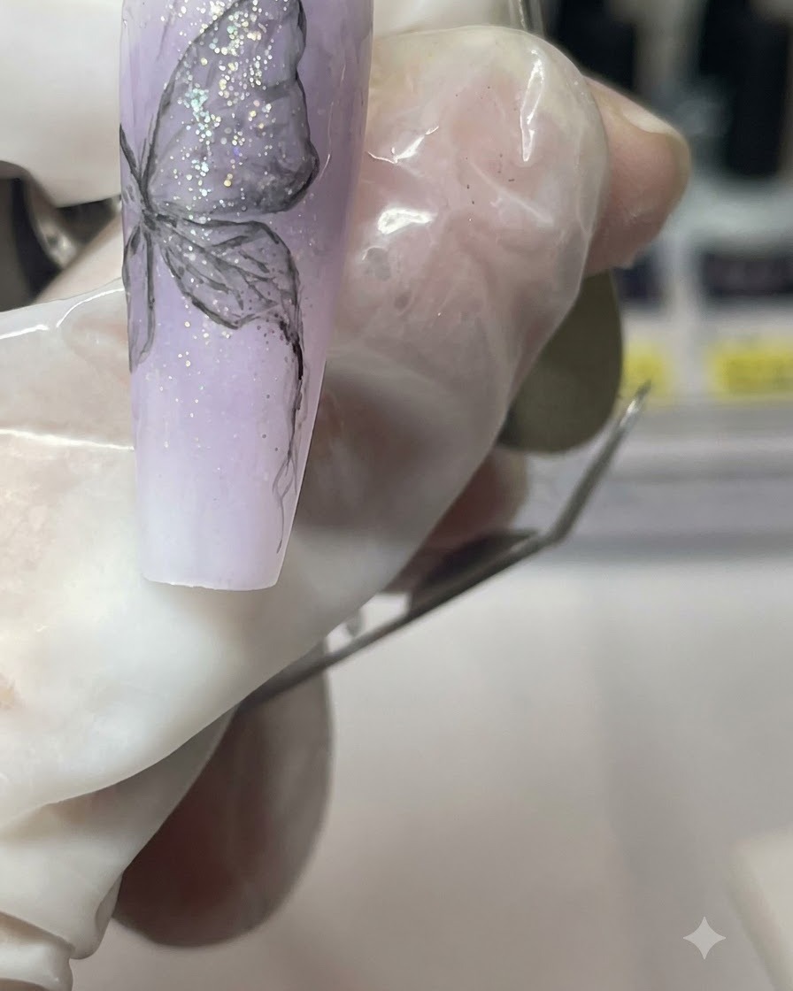 Nahaufnahme eines manikürten Fingers, der den lila Nagel hält, während der Schmetterlingskörper detailliert wird.
