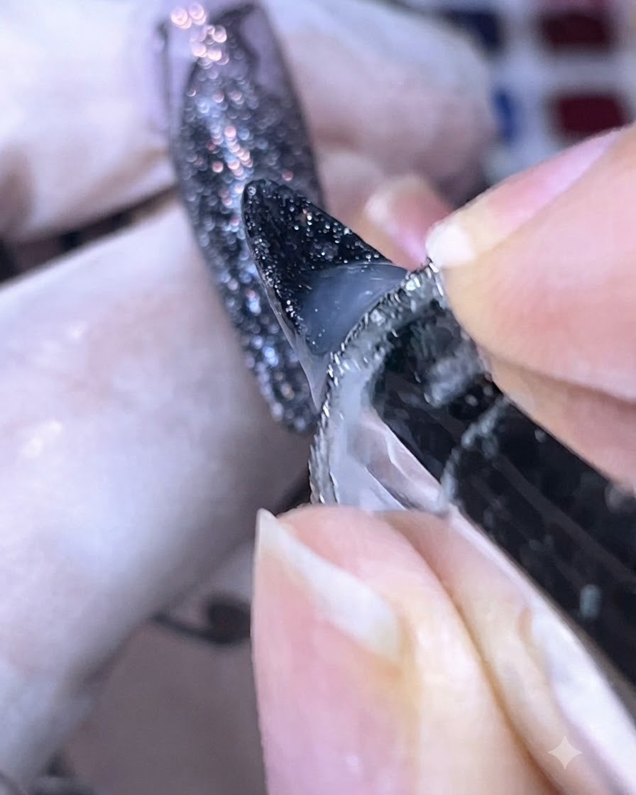Nahaufnahme vom Auftragen von Base Gel um die Ränder einer dunklen, glitzernden Nagelspitze.
