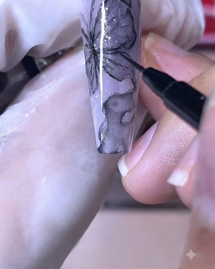 Ein feiner Nagelpinsel zeichnet scharfe schwarze Linien auf ein lila Schmetterlings-Nageldesign.