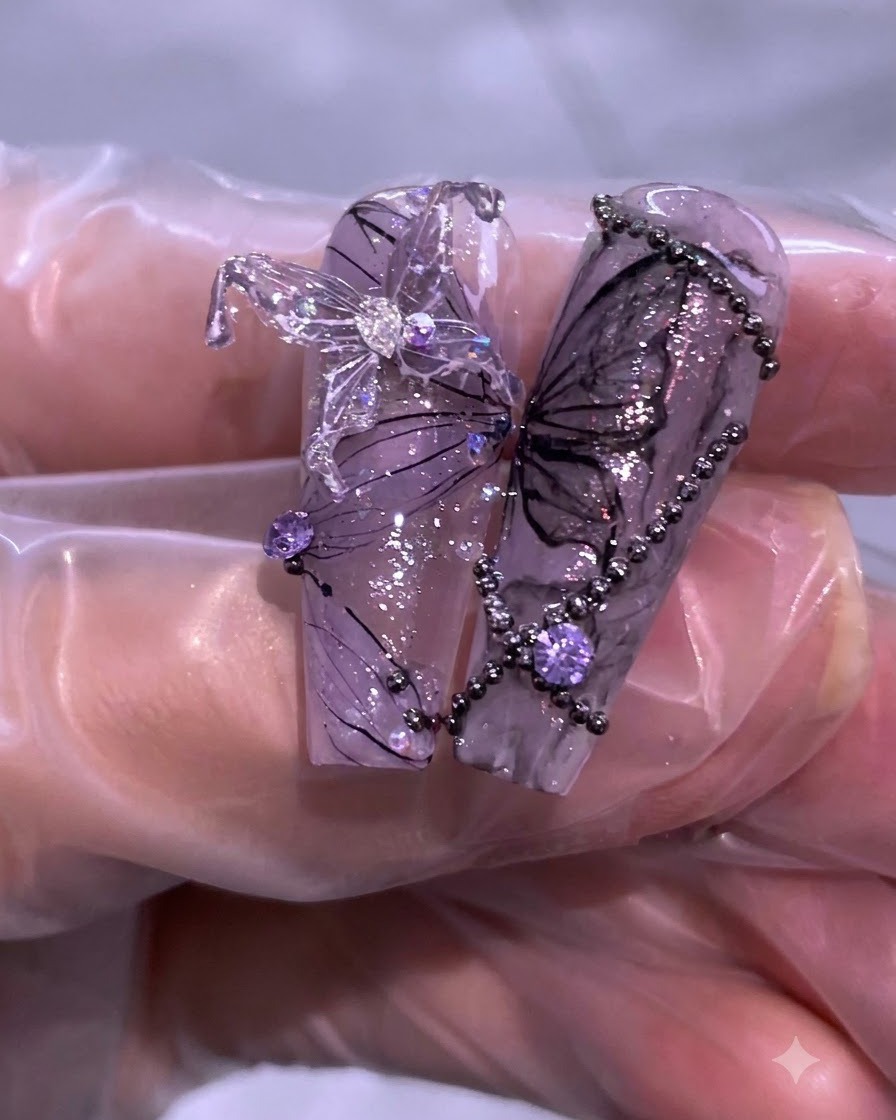 Nahaufnahme der fertigen lila-schwarzen Nailart mit Schmetterlingsdetails, Strasssteinen und zarten Fadenlinien.