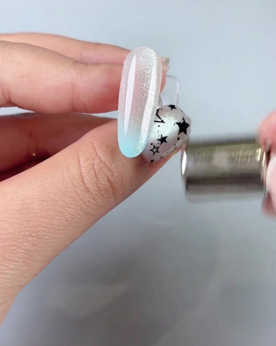 Ein Magnetstab wird nahe an die Seite eines Nagels gehalten, um ein breites Cat-Eye-Lichtband zu ziehen und zu formen.
