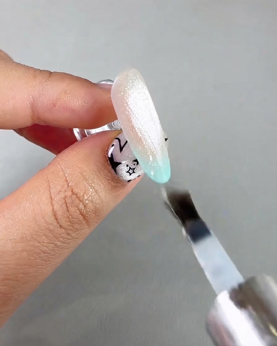 Ein Nagelpinsel trägt einen klaren Versiegelungstopcoat über einer schimmernden Cat-Eye-Nagelverlängerung auf.