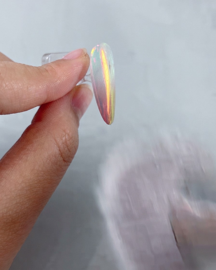 Ein weicher, flauschiger Pinsel fegt restliches Metallic-Puder von einem glänzenden Chrom-Finish-Nagel ab.