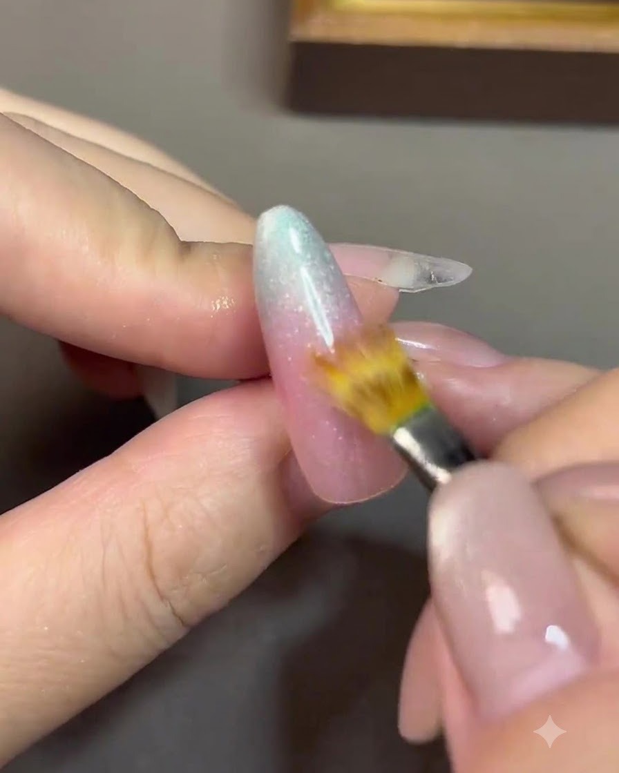 Ein feiner Detailpinsel verblendet die Übergangslinie zwischen einem Nude-Rosa-Gel und einem blauen Gel auf einem Nagel.